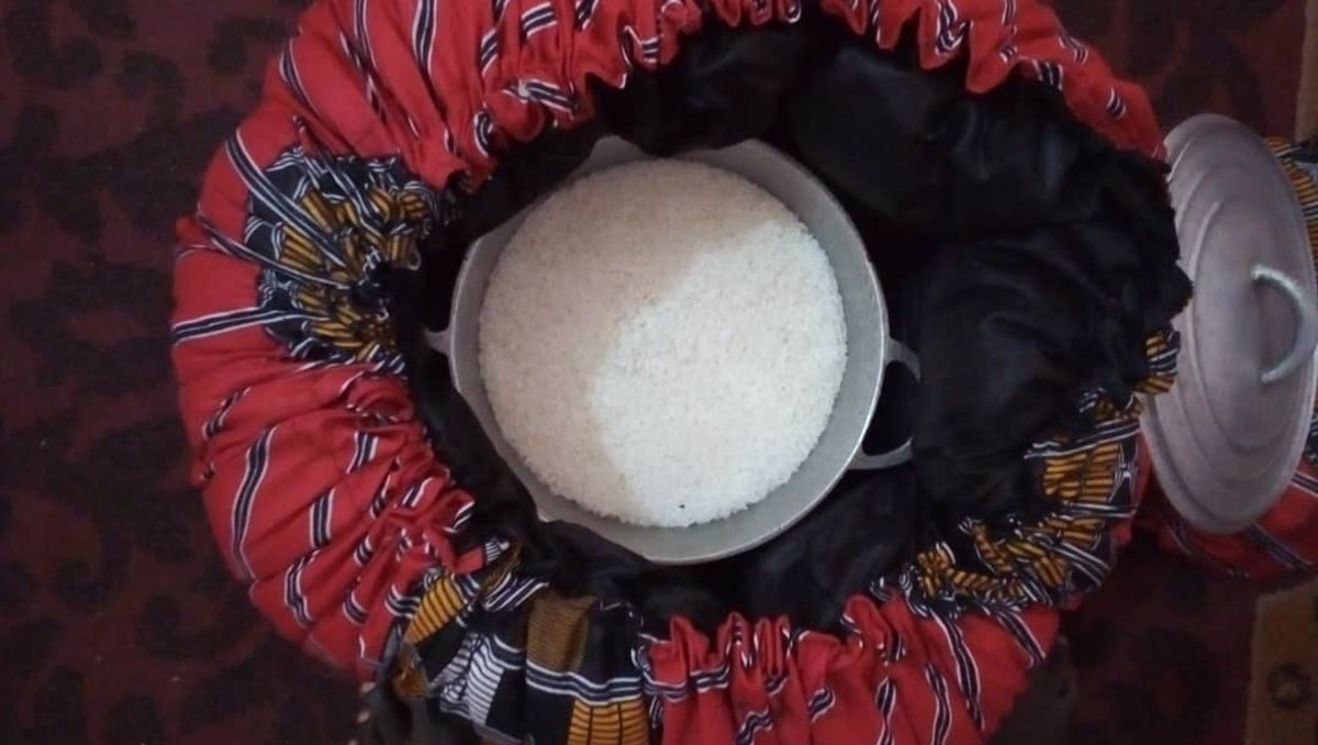 A red thermal cooker holds an open pot full of cooked white rice